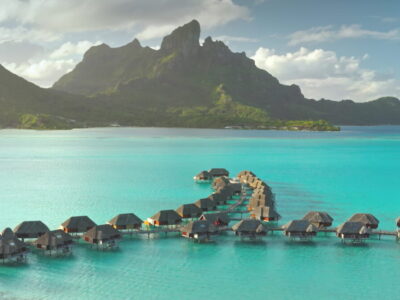 Aerial view overwater bungalows forming line towards mount Otemanu on tropical exotic Bora Bora island, with its turquoise lagoon and lush vegetation. Luxury travel vacation resort in coral reef ocean