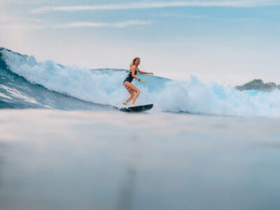 March 11, 2021. Bali, Indonesia. Surfer on surfboard and blue wave. Woman in ocean during surfing.