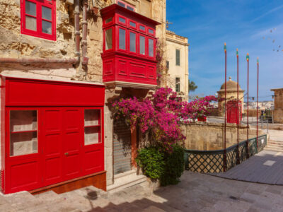 The traditional Maltese street with red phone box and building with colorful shutters and balconies at sunrise, Valletta, Capital city of Malta