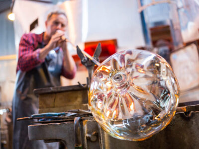Glassblower shaping a glass on the blowpipe at glassblowing factory