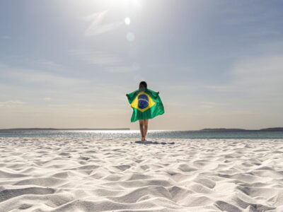 rear-view-woman-holding-brazilian-flag-standing-beach-against-sky
