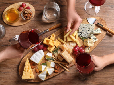 Women with glasses of wine and cheese plate on table, top view