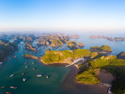 Aerial sunset view of Lan Ha bay and Cat Ba island, Vietnam, unique limestone rock islands and karst formation peaks in the sea, floating fishermen villages and fish farms from above. Clear blue sky.
