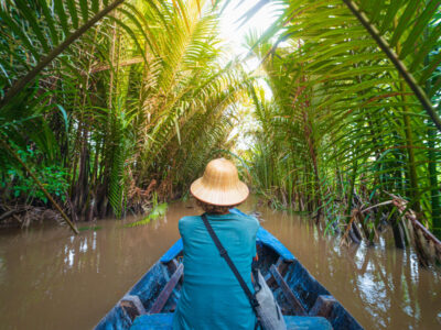 Boat tour in the Mekong River Delta region, Ben Tre, South Vietnam. Tourist with vietnamese hat on cruise in the water canals through coconut palm trees plantation.